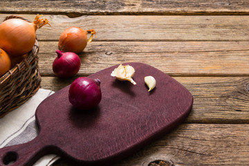 onions and garlics on cutting board, weathered wooden background
