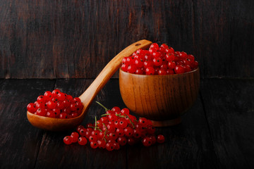 heap of red currant in wooden cup and in wooden spoon on black wooden background