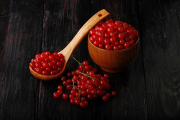 heap of red currant in wooden cup and in wooden spoon on black wooden background