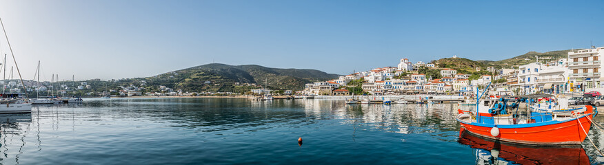 Obraz premium View of Batsi, a traditional village at the island of Andros, with a beautiful red fishing boat on the forground, Cyclades, Greece