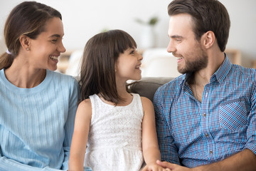 Smiling parents relax talking with little daughter