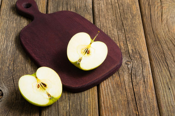 half cut green apple on chopping board, old wooden table