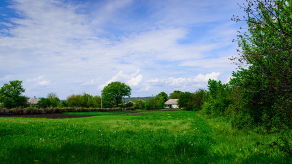 Landscape House in the village against the backdrop of green grass and blue sky