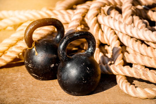 The concept of hard training in the gym, fitness and proper lifestyle. Two old scratched metal dumbbells on the floor on a background of ropes with glare from the sun. Closeup.