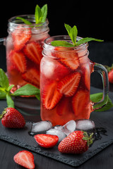Fresh strawberry smoothie. Fresh summer cocktail with strawberries and ice cubes on a dark background on a black wooden table...