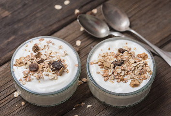Two glass bowls with white yogurt on old wooden desk with oatmeal on top.
