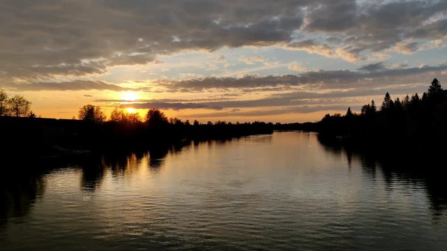 Sunlight through the orange horizon during the evening in northern Europe in a river bank with sky full of clouds in 4K