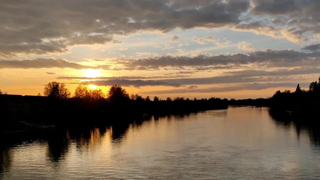 Sunlight through the orange horizon during the evening in northern Europe in a river bank with sky full of clouds 