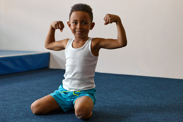 Portrait of happy cheerful dark skinned boy with short Afro hairstyle exercising at fitness center,...
