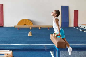 Horizontal image of skilled Afro American boy gymnast preparing for artistic gymnastics...