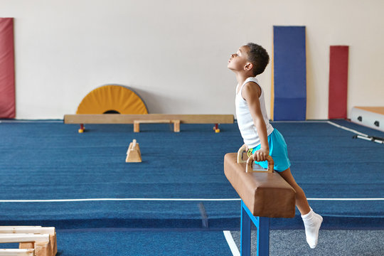 Horizontal image of skilled Afro American boy gymnast preparing for artistic gymnastics competition, exercising on pomme horse. performing difficult routine. Balance, strength and determination