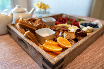 Wooden basket filled with various fruits, waffles and croissants and breakfast items