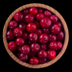 heap of cowberry in wooden cup isolated on black background. top view