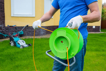 A man is connecting an electric extension cord on the coil in the house backyard.