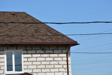 Fragment of the house of white foam blocks with a brown roof of roof tiles and a window.Construction