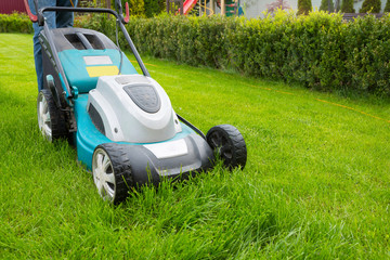 A man mowing grass with a lawn mower in the garden on a sunny day. A lawn mower on the lawn, a...