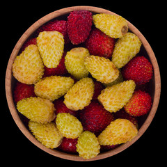 heap of red and yellow wild strawberry in wooden cup isolated on black. top view