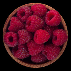 heap of red raspberries in wooden cup isolated on black background. top view