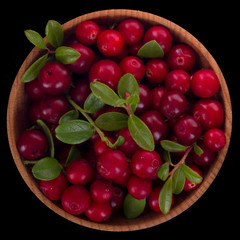 heap of cowberry with leaves  in wooden cup isolated on black background. top view