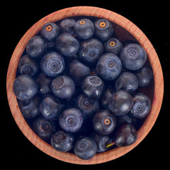 heap of bilberry in wooden cup isolated on black. top view