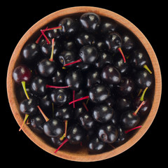 heap of black chokecherry in wooden cup isolated on black. top view