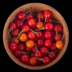 heap of red  solanum in wooden cup isolated on black. top view