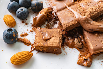 macro shot of a melted chocolate bar with almond nuts and blueberry on the white plates