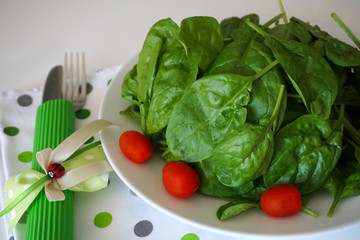 Baby spinach green leaves decorated with mini tomatoes, on a plate served for cooking or eating close up view
