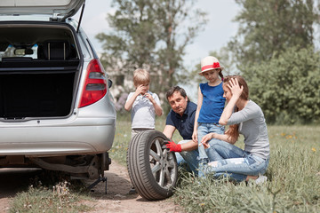 Plakat family with two children replace the tire of the family car.