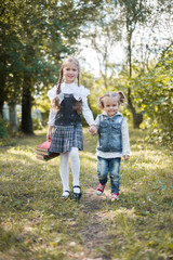 Fototapeta premium A schoolgirl walks in the park by the hand with her younger sister and carries books in her hand.