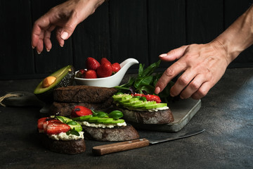 Healthy breakfast sandwich with avocado, cheese, strawberries, herbs and seeds on a dark background. An idea for bruschetta or for a healthy snack. Healthy vegan breakfast.