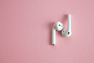 wireless white headphones without cord, lying next to each other on a pink background. Place for...
