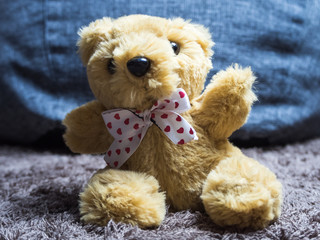Soft toy fluffy bear with a bow around his neck sits on the carpet