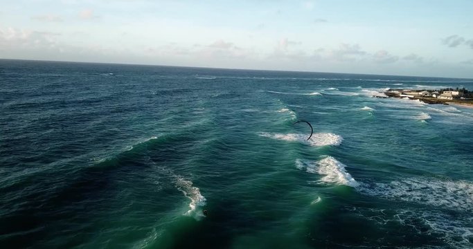 Aerial view, kite surfer riding the waves in front of Barbados, coastline on the right side.