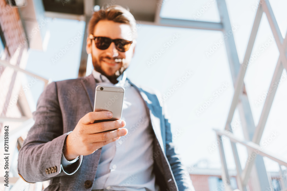 Wall mural young handsome businessman with stubble and sunglasses walking down the stairs outside. smiling and 