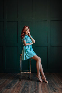 Redhead Girl In Short Dress With Beautiful Long Legs Sitting On Chair On Dark Background