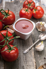 Ketchup or tomato sauce, garlic and fresh tomatoes on a branch on a rustic background.