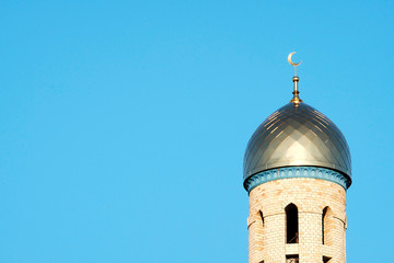 The Golden minaret of the mosque. Muslim symbol on blue sky background. Crescent. Sunset. The concept of religion.