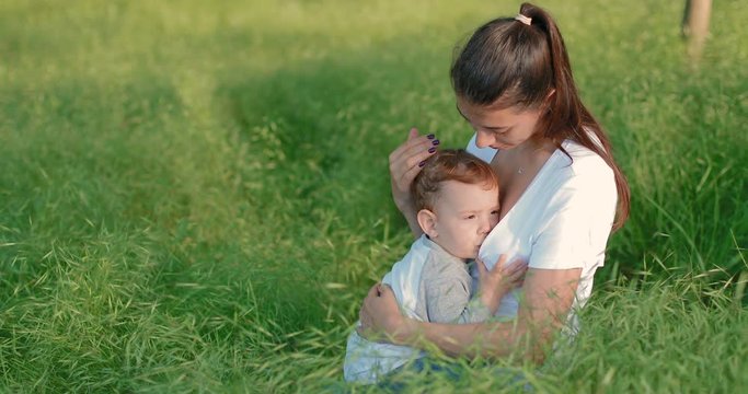 Young mother breastfeeds her one year old baby while sitting in a park on green spring grass. in slow motion. Shot on Canon 1DX mark2 4K camera