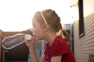 A little girl blowing soap bubbles in summer park.