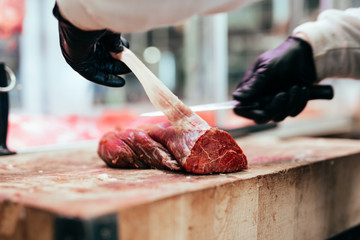 Butcher cutting meat at counter in butchery.