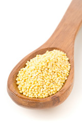 Pile of golden millet, a gluten free grain seed, in wooden spoon over white