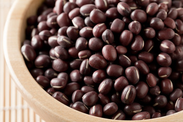Raw, uncooked, dried adzuki (red mung) beans in wooden bowl on bamboo mat background
