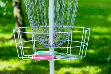Metal golf basket in the grass and trees in the middle of the park. Basket used to play frisbee...