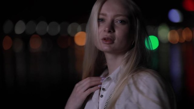 Beautiful blonde woman model with long hair posing in the night city, slow motion