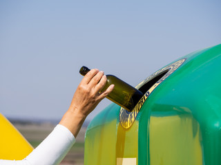 A mature woman pulling a crystal bottle in a green bin for recycling glass with the spanish text "only glass containers"