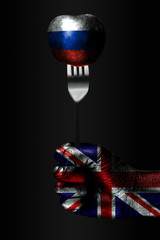A hand with a drawn Great Britain flag holds a fork, on which is a ball with a drawn Russia flag, a...
