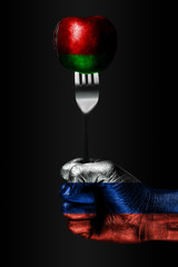 A hand with a drawn Russia flag holds a fork, on which is a ball with a drawn Belarus flag, a sign...