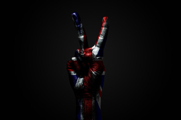 A hand with a drawn Great Britain flag shows an PEACE sign, a symbol of peace, friendship, greetings and peacefulness on a dark background.