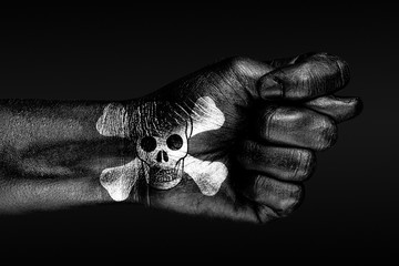 On a hand with a painted human skull and bones depicted a fig, a sign of aggression, disagreement, piracy, on a dark background.